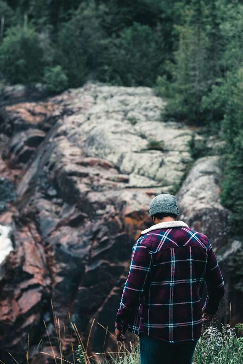 man in red and black checkered dress shirt standing on rocky mountain during daytime