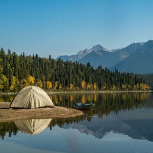 white tent on lake near green trees and mountain under blue sky during daytime